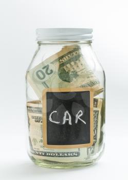 Glass jar on white background with black chalk label or panel and used for saving of US dollar bills for car expenses