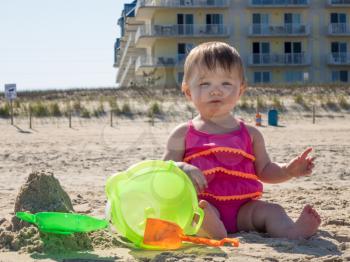 Cute caucasian baby girl on sandy beach tasting sand for the first time in Ocean CIty, Maryland, USA