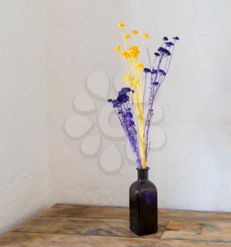 Purple and yellow dried flowers in blue bottle as a vase on an old wooden table or bench