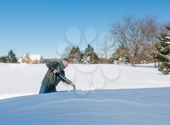 Senior man with snow shovel looking at snow drifts on driveway as he tries to dig out from the blizzard