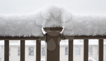 Heavy snow forms a peak and ridge on top of the balcony railing of a deck with houses behind
