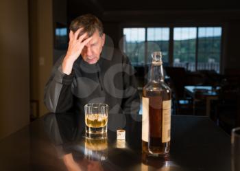 Senior adult male facing a kitchen table with alcoholic drink and looking very sad and depressed