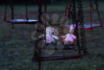 Halloween image of an abandoned childs dolly and small soft toy of girl on old rusty swing at fun fair