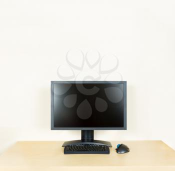 Plain light colored wooden desk with computer monitor and keyboard to suggest calm, organization and meditation at work or in home office