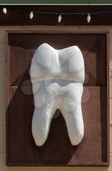 Large carved white painted wooden molar tooth on wall outside dentist surgery
