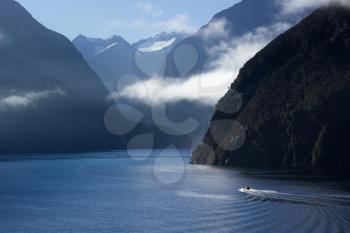 Sailing into Milford Sound on South Island of New Zealand in early morning as the sun rises above the mountains