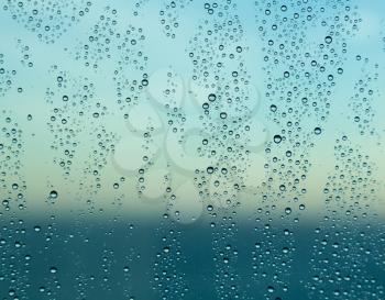 Blue color of ocean behind rain or spray drops on window of cruise ship as the sun starts to rise at dawn and illuminate the water