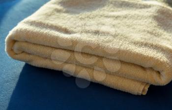 Folded stack of yellow bath or beach towels with the sun shining on the pile from the side giving a warm glow to the toweling which is sitting on a soft blue cushion or bed