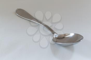 Decorated serving or dessert spoon for  vegetables in side view on fine white tablecloth with pattern just visible