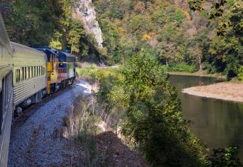Diesel locomotive engine on steep trip into mountains of West Virginia with fisherman in the calm river below the tracks