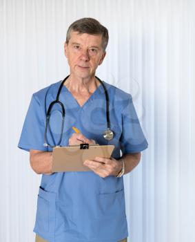 Senior male caucasian doctor with stethoscope in medical scrubs and confidently facing the camera in portrait