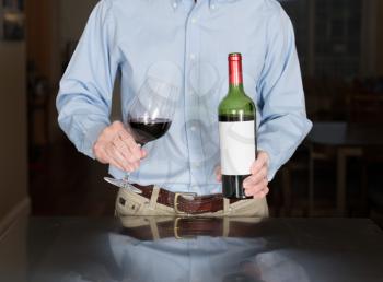 Senior caucasian man standing in kitchen pouring from bottle of red wine with a blank label for copy space