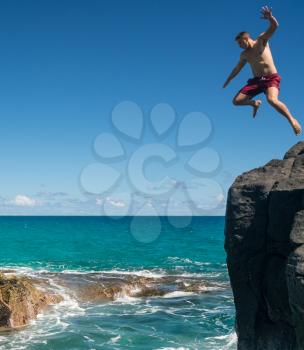 Dangerous leap into warm blue ocean off rocks at Lumahai Beach on Hawaiian island of Kauai