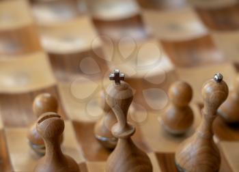 Macro focus on the cross on top of the king piece of chess set with carved wooden pieces