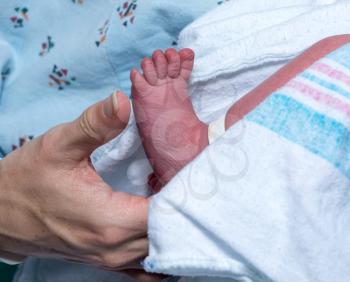 Mother in hospital bed holding the tiny foot of newborn son or daughter