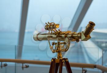 Brass antique optical telescope on deck of cruise boat looking out through windows