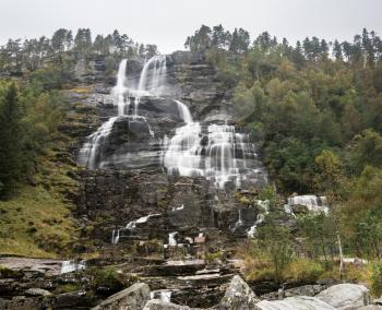 Cascades of water fall down hillside at Tvindefossen waterfall near Voss in Norway