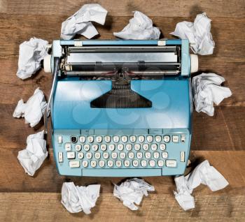 Modern electric typewriter on wooden desk background with papers ready for a new book or novel with many failed pages screwed up on desktop