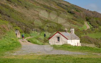 Hikers near a stone cottage on coastline near Hartland Quay on North coast of Devon