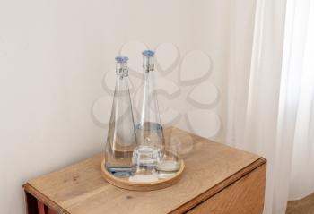 Still and sparkling water in glass bottles on tray in hotel bedroom on wooden table