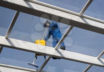 Male worker washing large expanse of glass roof over swimming pool