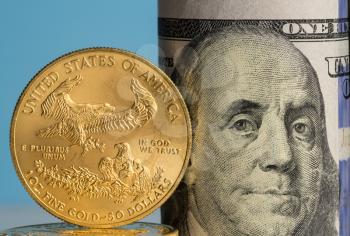 Pure gold eagle coin in front of Benjamin Franklin face on rolled bankrolls of USA dollar bills