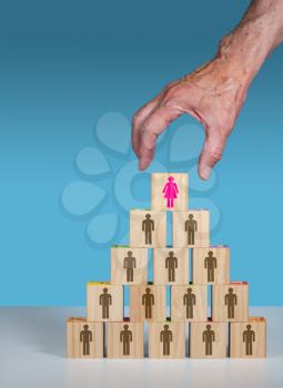 Older mans hand placing a woman CEO or leader at the top of an organization chart made from blocks