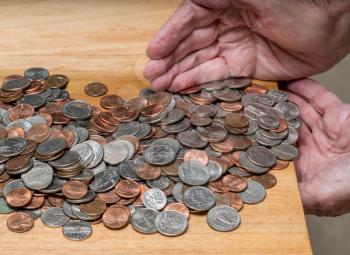 Hundreds of US coins being gathered into hands on wooden table as concept for hoarding during shortage of loose change