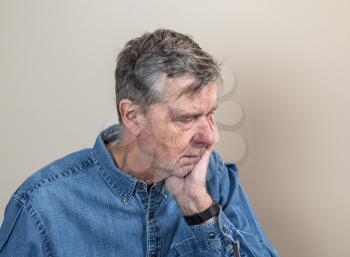 Head and shoulders portrait of a senior caucasian man with head in hands and looking depressed