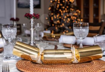 Traditional british christmas lunch table setting with crackers and glasses with xmas tree in the background