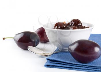 Ripe plums, jam and spoon on white background