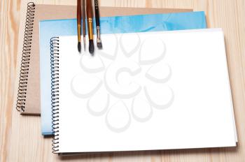 Notebooks and brushes on a wooden background