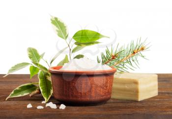 Aromatic bath salt in a clay cup, soap and green leaves on a wooden background