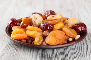 Dried fruits on a wooden background. Dates, lemon, apricots, figs and nuts in a clay plate. 