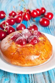 Fresh homemade bun with sweet cherry on a blue wooden background