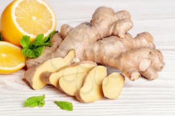 Fresh sliced ginger root, lemon and green mint leaves on a wooden background. Ingredients for ginger herbal tea