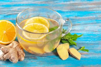 Glass cup of hot ginger tea with lemon and peppermint on a blue wooden background. Winter herbal drinks concept