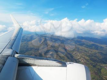 Wing of the plane on blue sky, clouds and mountains background