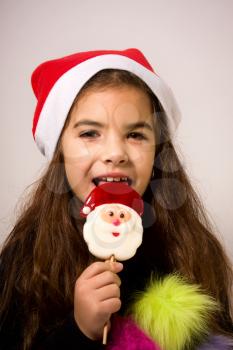 A little girl in a New Year's hat eating a candy in the form of Santa Claus