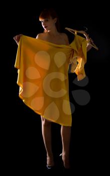 beautiful naked girl on a dark background examines and tries on herself a yellow dress on a hanger