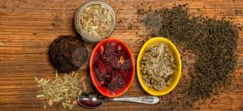 several traditional oriental teas in containers and scattered on a wooden background