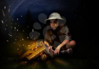 a little girl in a tropical uniform and a cork helmet sits at night by the fire and blows the sparks