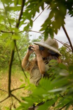 a little girl in a tropical khaki uniform and a cork with binoculars looking for adventures in nature