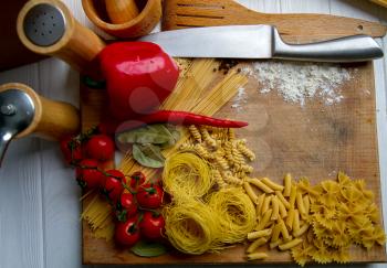 background from dry pasta and vegetables for making sauce with spices and kitchen utensils lying on the kitchen table top view