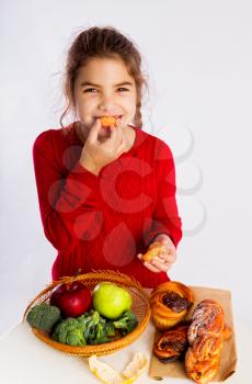 Little girl chooses what to eat, healthy food or buns