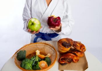 A little girl in karate uniform and a blue belt chose apples to eat instead of bread rolls.