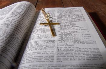 Open holy bible close up and a small metal cross on a chain