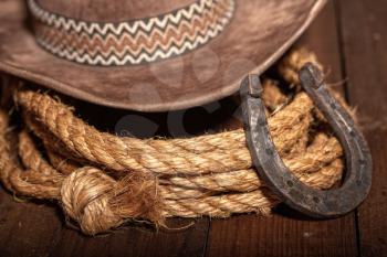 An old horseshoe lies next to a classic cowboy hat and lasso on a dark wooden background.