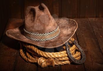 An old horseshoe lies next to a classic cowboy hat and lasso on a dark wooden background.