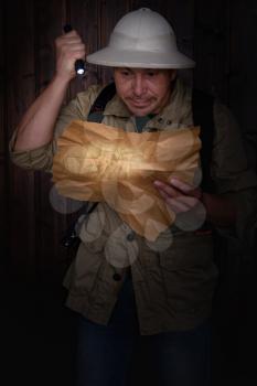 a traveler in a cork helmet and khaki clothes looking at an old map highlighting a flashlight